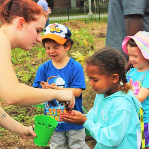 A college student places dirt into the hands of a young girl