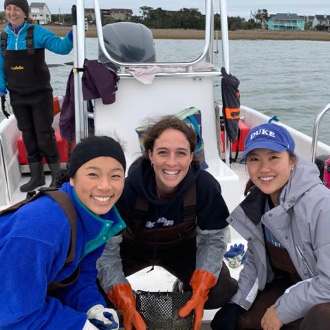 Three students on a boat holding a bag of oysters