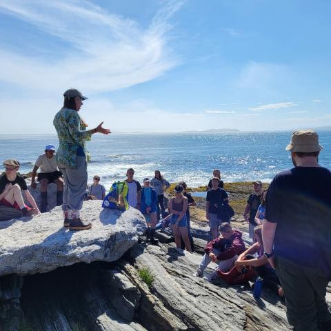 A group of students and a professor on a rocky shoreline in Maine.