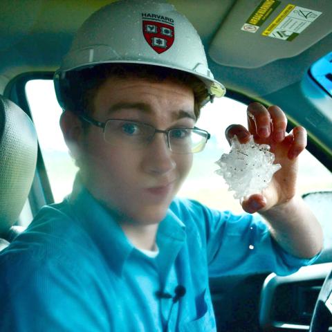 A man sits in a pickup truck holding a large piece of hail.