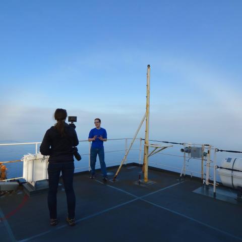 A man stands on a ship with a rainbow in the background