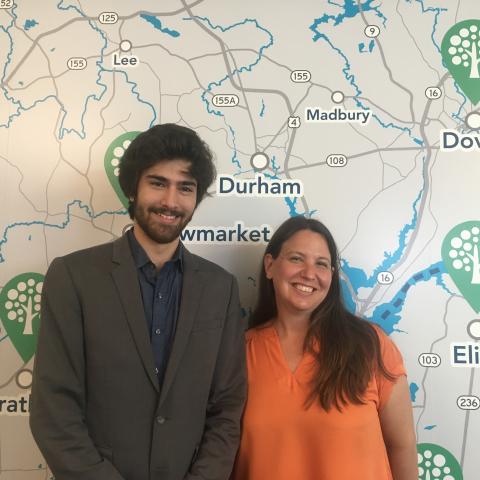 Two people stand in front of a map of New Hampshire