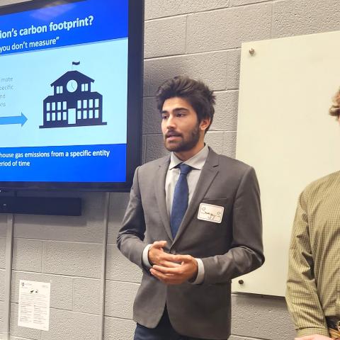 Two students stand in front of a screen presenting information