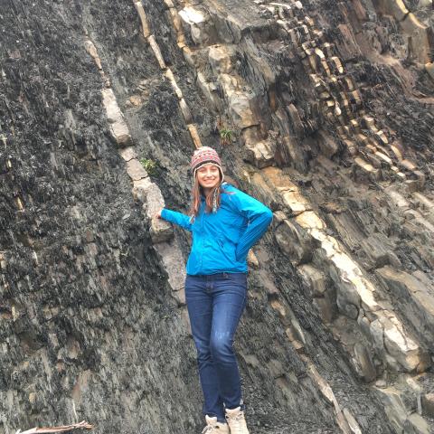 A young woman stands at the bottom of a steep cliff