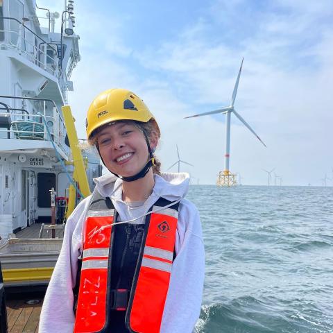 A woman on a large ship on the ocean with a wind turbine in the background
