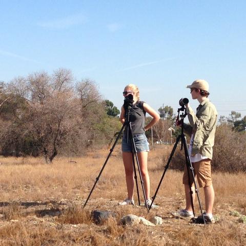 Two students standing in a field of scrub brush using scientific equipment