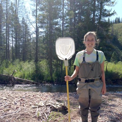 A young woman stands with a fishing net on a riverbank