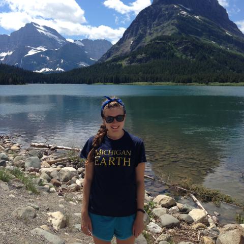 A woman stands in front of a glacial lake