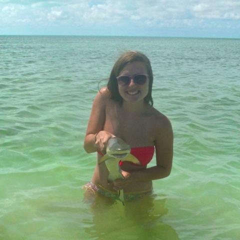 A young woman stands in the ocean and holds a small shark