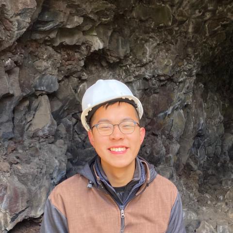 A young man in a hardhat in front of a cave