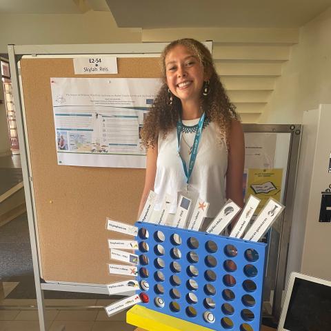 A woman stands behind a Connect 4 board used to demonstrate scientific research