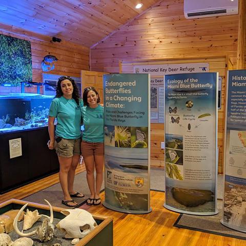 Two women stand in a museum next to exhibit panels on the blue butterfly