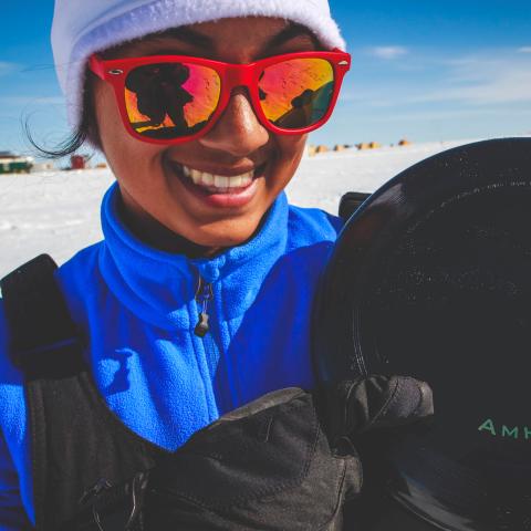 A woman stands in a field of Arctic snow and holds a camera