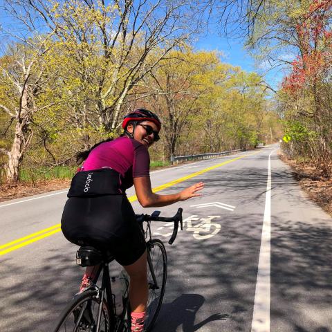 A woman on a bike rides down a road in springtime