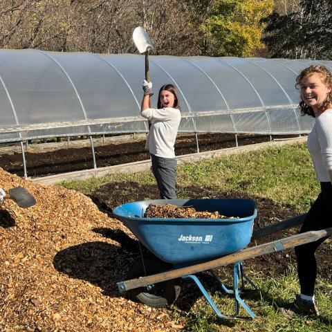 Three students shoveling mulch. One pushes a wheelbarrow.