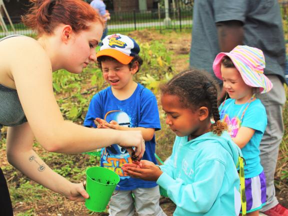 A college student places dirt into the hands of a young girl