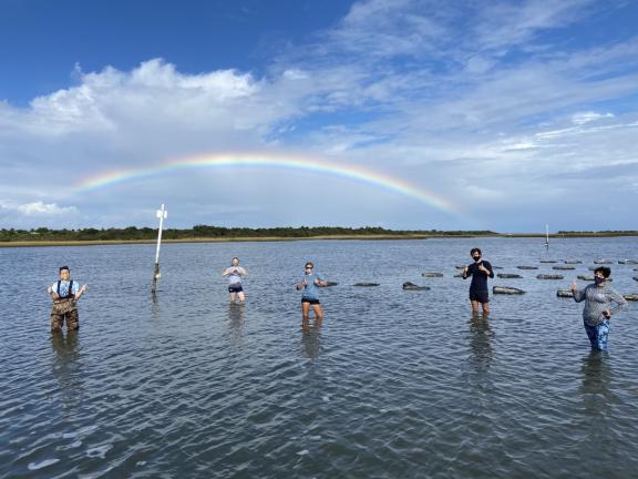 Students stand in the ocean with a rainbow in the background