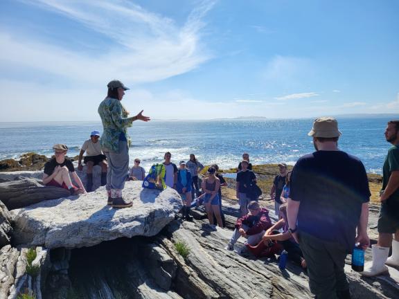 A group of students and a professor on a rocky shoreline in Maine.