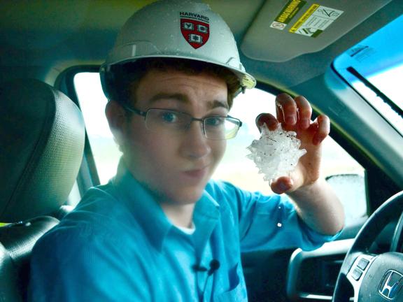 A man sits in a pickup truck holding a large piece of hail.