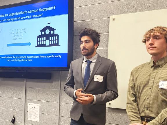 Two students stand in front of a screen presenting information