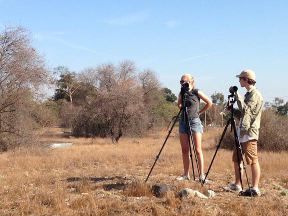 Two students standing in a field of scrub brush using scientific equipment