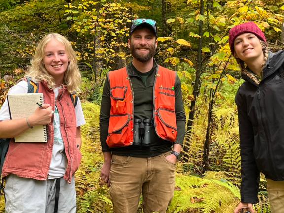 Three people standing in a forest.