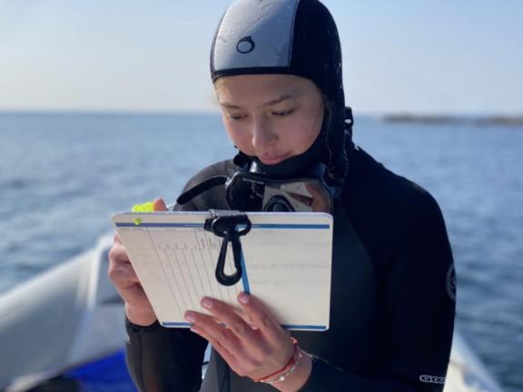 A young woman in a wet suit takes scientific notes