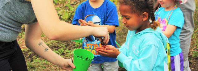 A college student places dirt into the hands of a young girl