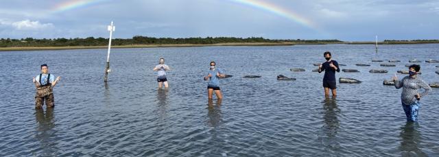 Students stand in the ocean with a rainbow in the background
