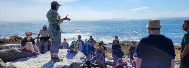 A group of students and a professor on a rocky shoreline in Maine.