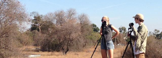 Two students standing in a field of scrub brush using scientific equipment