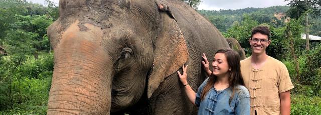 Two college students pet an elephant